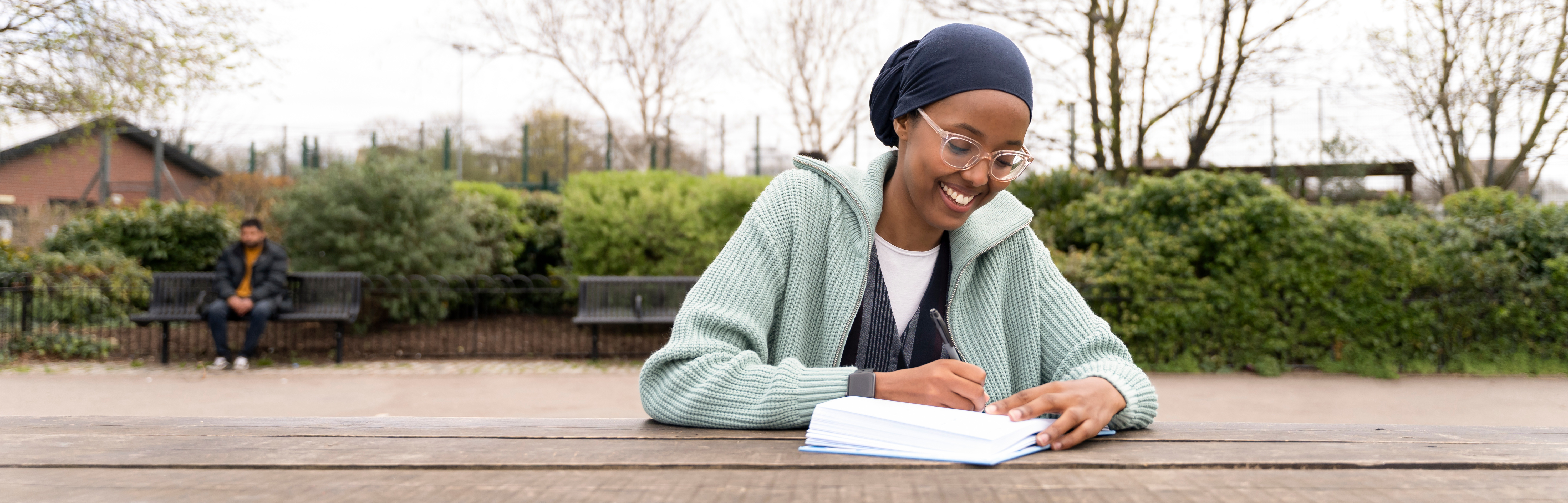 A student sits outside journaling at a picnic table.