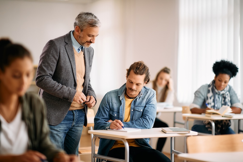 A professor talking to a student who is pointing at a notebook.