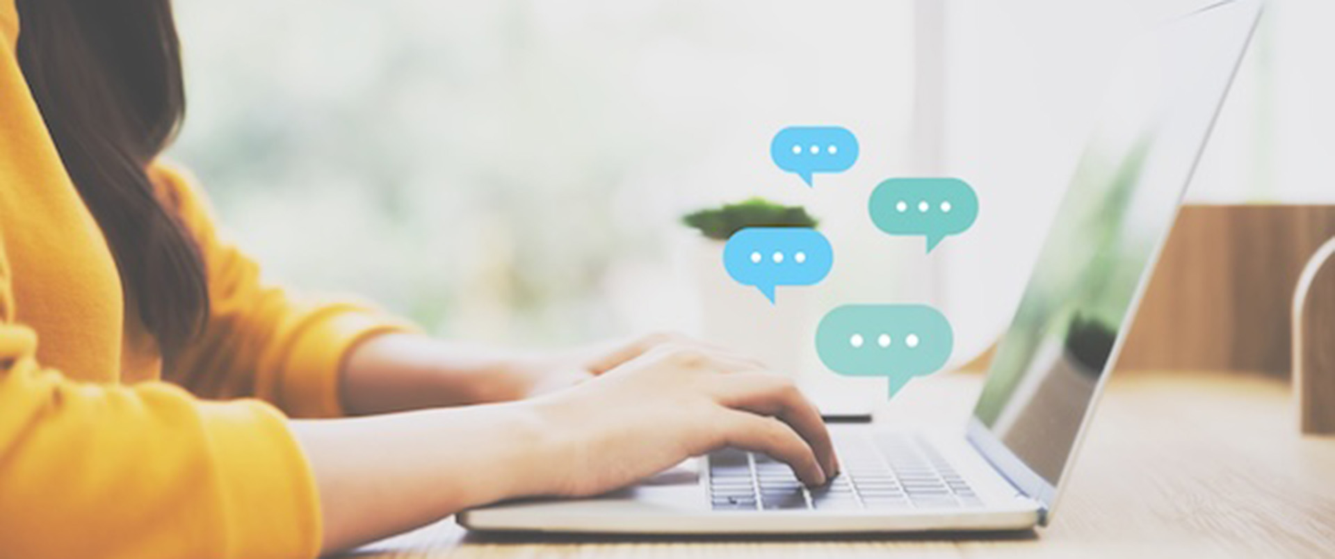 Side view of a hands typing on a laptop with conversation bubbles popping up. 