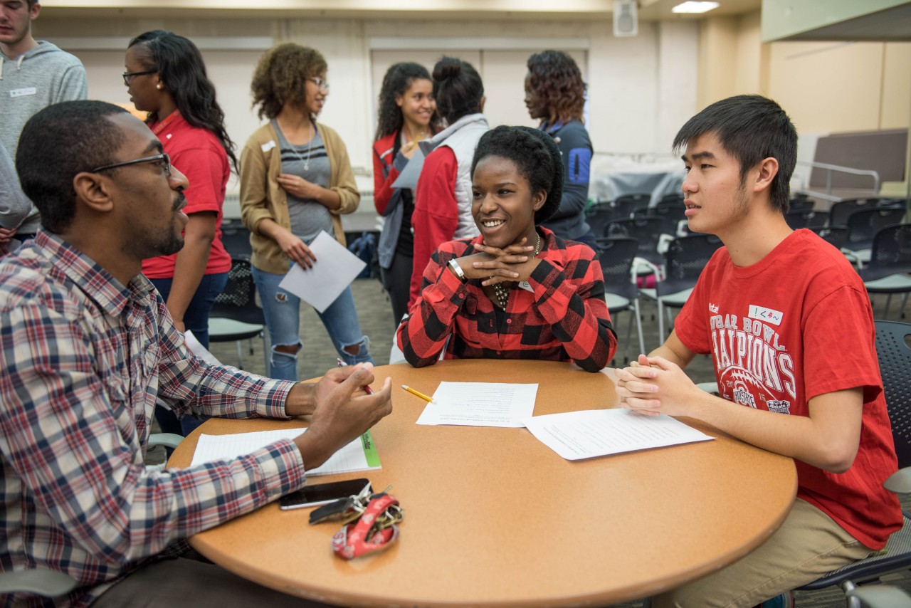 An instructor leads a small group discussion while more students talk in the background.