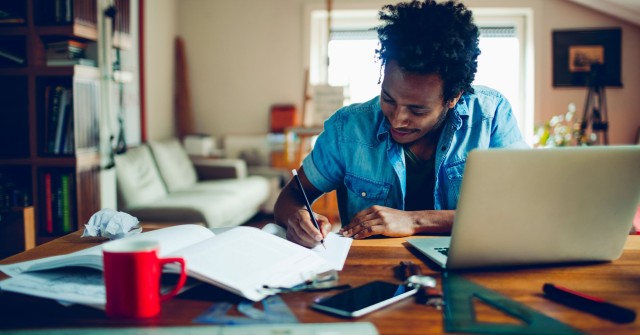 Male student writing next to a laptop