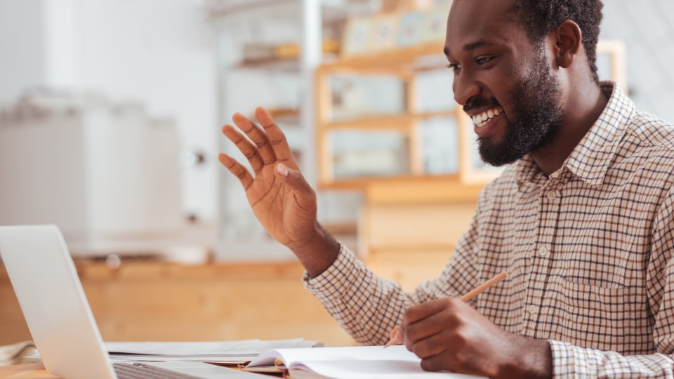 Man smiling and waving to computer screen