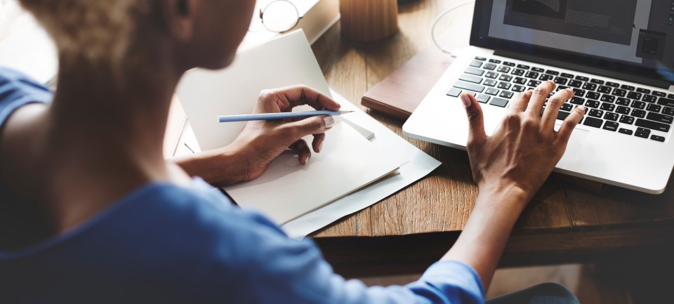 Woman writing and looking at laptop. 