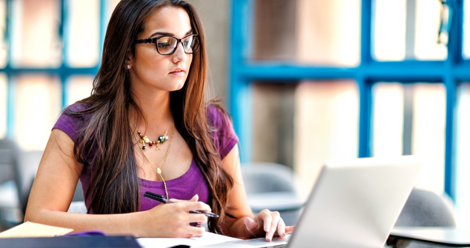 Woman with dark hair and glasses working on laptop