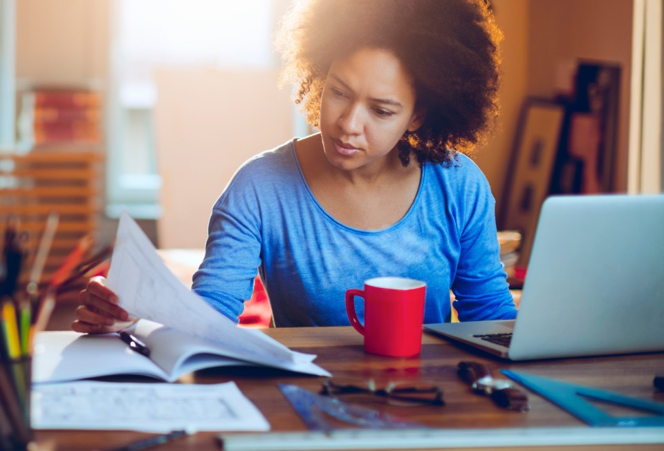 Woman with laptop reviewing papers.