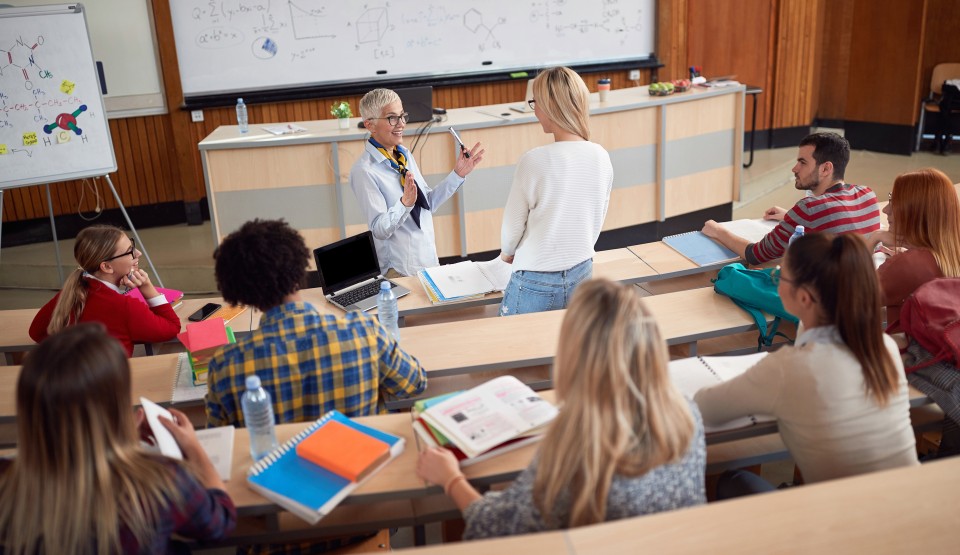 An instructor speaks to a student at the front of a lecture hall.