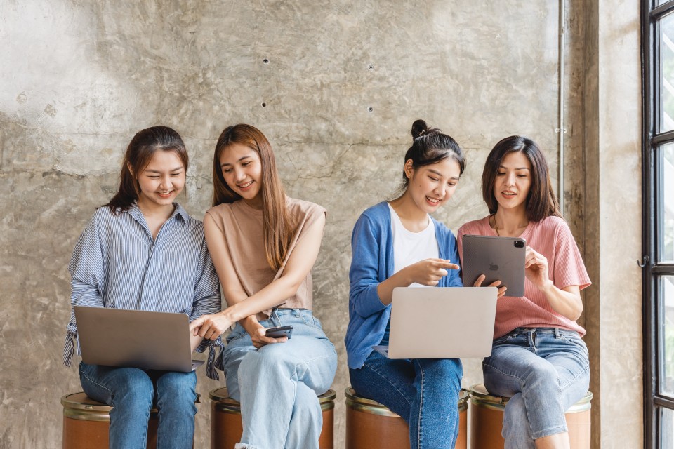 Four students with laptops, a phone, and tablets share content.