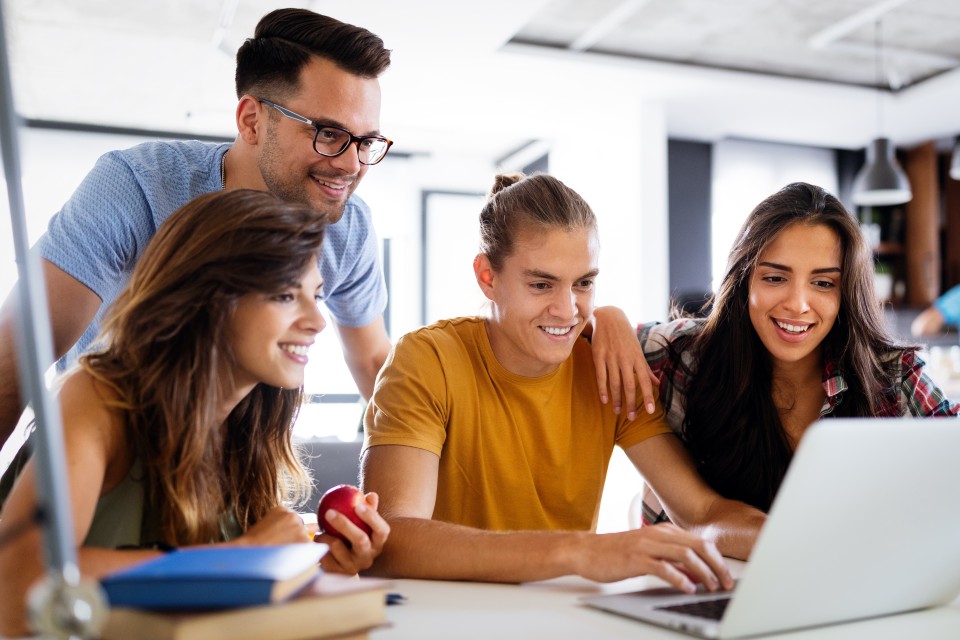 Students gathered around a laptop, smiling.